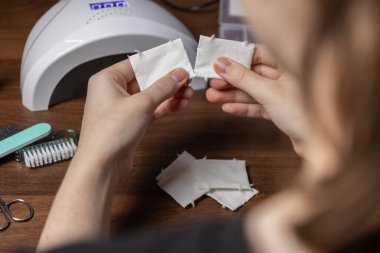 Ellerin ahşap bir masanın üzerindeki pamuk bloknotları titizlikle yırtıp jel cilası uygulaması ve kaldırılması için kişisel bakım araçlarıyla çevrili olduğu yakın çekim görüntüsü.