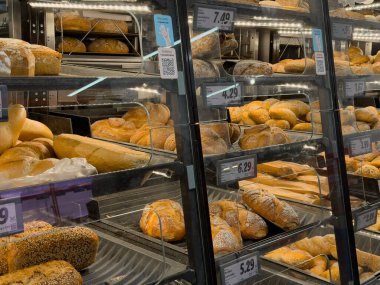 Poznan, Polonya - 29 Ekim 2025: Canlı bir süpermarket pastanesinin çeşitli sıcak ekmek, rulo ve ekmeklerle dolu cam rafları müşteriler için hazır olan yakın görüntüsü