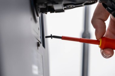 Kırmızı bir tornavidayı sıkıca kavrayan bir işçinin eline yakın plan. Metal bir desteye siyah bir vida takmak için. Odaklanma, uzmanlık ve el işi.