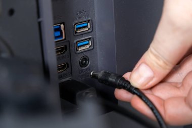 USB ve HDMI portlarını çok yönlü elektronik bağlantı için kullanan bir cihazın arkasındaki DC-IN portuna bir güç kablosu bağlayan elin yakın çekimi