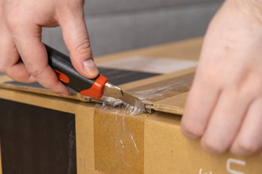 Kişi kahverengi karton kutuda bıçak ile temiz bant keser, modern e-ticaretin altını çizer, etkin lojistik ve boks olmayan heyecan verici ürün