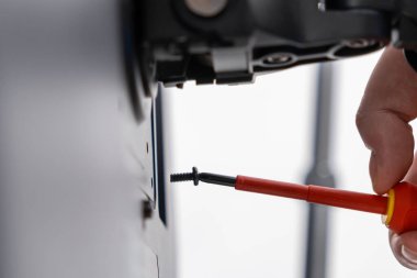 Yakından çekimde, yalıtılmış bir tornavidayı kullanarak bir vidayı bileşene sağlam bir şekilde yerleştiren bir işçi eli görülüyor. Onarım ve teknik hassasiyet göstermek için mükemmel.