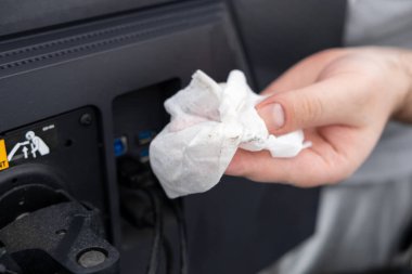 Siyah bir bilgisayar ekranının arkasındaki tozları titizlikle temizleyen kirli beyaz bir bezle bir insanın eline yakın çekim yapmak, teknik bakımın öneminin altını çiziyor.