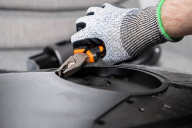 Kara makine parçalarını dikkatlice monte etmek için turuncu pense kullanarak işçinin eldivenli elinin yakın çekimi, endüstriyel onarım ve profesyonel bakım görevlerini vurguluyor