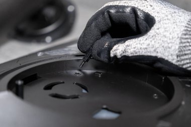 Yetenekli bir işçinin eldivenli eli titizlikle siyah elektronik bir bileşene kritik vida açmazı yerleştiriyor. Detaylı onarım ve uzman imalatına işaret ediyor.