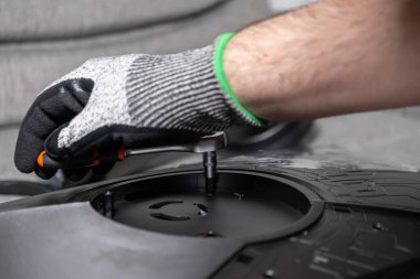 Karanlık bir elektronik cihazın vidalarını sıkmak için bir İngiliz anahtarı kullanan bir işçinin eldivenli elinin yakın çekimi, dikkatli montaj, teknik uzmanlık ve karmaşık bakım işleri gösteriyor.