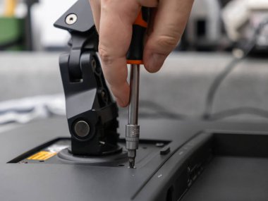 Siyah bir bilgisayar monitörünü güvenli bir şekilde takmak için turuncu ve siyah bir tornavida kullanan birinin elinin yakın plan çekimi, ofis kurulumu ve ekipman bakımı için hayati önem taşıyor.