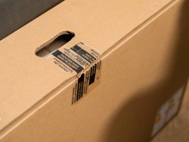 Sıkı bir taşıma kolu ve çok dilli güvenlik bandıyla kahverengi bir nakliye kartonunun yakın çekimi, dikkatli ürün denetimi ve çevrimiçi alımlar için güvenli teslimat vurgulanması