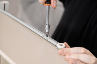 Yüksek açılı yakın çekim vitrinleri elleri titizlikle açık renkli mobilya paneline sürgülü çekmeceyi yerleştiriyor ve ev yapımı DIY montajdaki hassasiyeti vurguluyor.