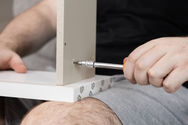 Ellerinizi sıkıca vidalarken açık renkli ahşap mobilya paneline tornavida takın. Pratik ev yenileme ve kendiliğinden montaj becerileri sergiliyorsunuz.