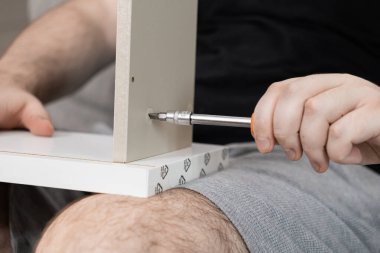 Mobilya paneline vida takmak için tornavida kullanan bir elin yakın çekimi, ev yenilemesi, kendin yap ve kişisel montaj.