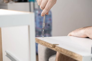 Beyaz parçacık tahtası mobilyalarını özenle monte eden, DIY ev geliştirme ve zanaatkarlık sürecini gözler önüne seren bir kişinin ellerinin ayrıntılı görünümü