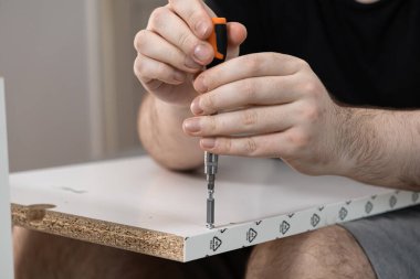 İç montaj ve inşaat sürecini vurgulayan, tornavidayla vidayı parçacık tahtası mobilyasına sıkıştıran ellerin detaylı görünümü