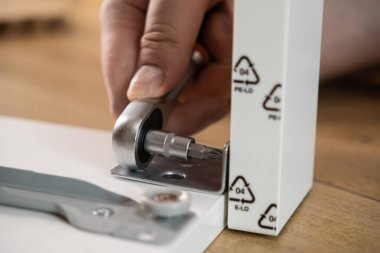 Cırcır anahtarıyla yakın plan bir el, yeni beyaz mobilya parçasına metal bir deste takmak, pratik ev yenilemesi ve detaylı inşaat işleri.
