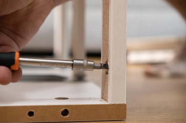 Montaj projesine özgüveni vurgulayan, önceden delinmiş bir parçacık tahtası parçasının delinmiş deliğine vidayı ustalıkla sokan elin detaylı yakın çekimi