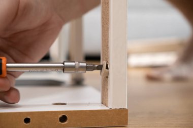 Bir el ve aletin yakın plan çekimi modern parçacık tahtası mobilyalarını bir tornavida ile sağlamlaştırmak, kendi kendine montaj, işçilik ve ev eşyası çalışmalarını temsil etmek.