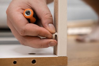 Bir insanın elinin yakın plan çekiminde plastik mobilya kamerası yerleştirirken ahşap bir tahtanın içindeki önceden delinmiş bir deliğe yerleştirilirken ayrıntılı elle montaj ve DIY işçiliğini vurguluyor.