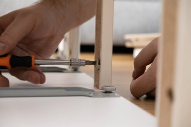 Düz paket mobilya parçasına tornavidayla vida takan bir insan elinin detaylı görüntüsü, modern DIY montaj, yetenek ve dikkatli ev geliştirmesi.