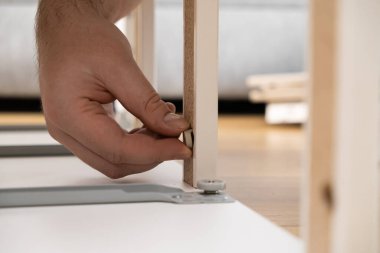 Ev mobilyası montajı sırasında ahşap bir panelin ön delinmiş deliğine küçük beyaz plastik bir panel yerleştiren yetişkin bir elin detaylı görüntüsü bireysel becerilerini gösteriyor.