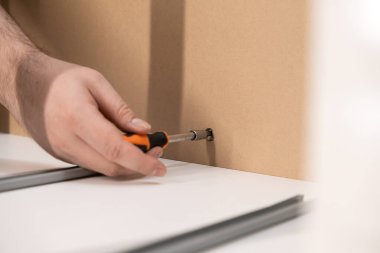 Elinde tornavida olan bir elin yakın plan görüntüsü kahverengi bir mobilya tahtasına vida takarken özgüven, el işi ve modern iç dekorasyonu vurguluyor.