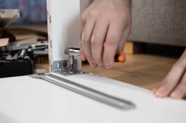 İnsan ellerinin ev mobilyaları montajını yapması, metal bir desteğin vidasını mandalla sıkması, kendini işine adaması ve pratik ev geliştirmesi.