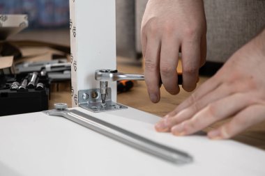 Bir insanın ellerinin yakın plan modern beyaz mobilyaları kilit anahtarıyla dikkatlice monte etmesi, DIY ev yenileme projesinin bir parçası olarak metal bir parantez takması.