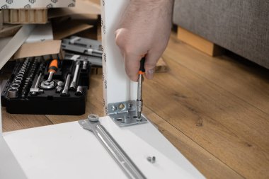 Beyaz bir mobilya parçası için tornavidayla vidayı sıkan bir kişinin eli yakın plan, ev yenileme ve kendiliğinden montajı temsil ediyor.