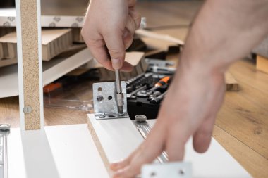 Bir insanın elleri, mobilya montajı sırasında titizlikle donanım kurarken, metal bir parçayı parçacık tahtasına vidalarken, modern ev yenileme sürecini ön plana çıkarırken görülüyor