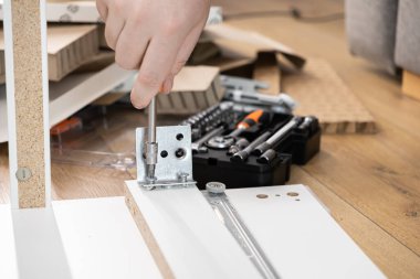 Tornavidayla bir elin yakın çekimi, yeni beyaz düz paket mobilya bileşenine metal bir deste takmak, ev montajı, onarım ve pratik DIY becerilerini göstermek,