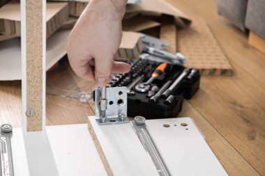 Yetenekli bir elin, beyaz parçacık tahtasına metal bir desteyi dikkatlice vidalaması, mobilya montajı ve evdeki yenileme görevlerini gözler önüne sermesi,