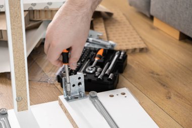 Bir adamın eli titizlikle yeni düz paket mobilyaların bileşenlerini düzerken, ev yenileme, montaj ve bakım projesini sembolize ediyor.