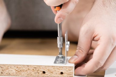 Tahta bir tahtaya metal bir deste takmak için tornavida kullanan odaklanmış eller pratik DIY becerilerini, ev geliştirmeyi ve montajı vurguluyor.