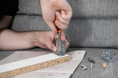 Kullanım kılavuzunu takip eden ellerin yakın plan görüntüsü metal bir köşe desteğini dikkatlice tahta bir mobilya paneline vidalayarak pratik DIY becerilerini temsil ediyor.