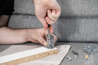 Erkek ellerinin yakın plan görüntüsü, yeni bir parçacık tahtası rafına metal bir parantez bağlıyor, bir kağıt kılavuzu ile, ev mobilyalarını ve DIY montaj sürecini temsil ediyor.