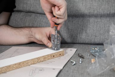 Bir tornavidayla düz paket mobilyaları dikkatlice birleştirirken, ev geliştirme, el işi ve kendine güvenme sürecini gösteren odaklanmış bir fotoğraf.