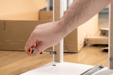 Beyaz düz paket mobilya monte eden turuncu bir tornavidayla el, ev yenileme, DIY projeleri ve yeni bir iç çevre inşa etmenin memnuniyeti vurgulanıyor