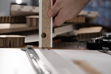 Yeni düz katlı mobilya montajı üzerinde çalışan, panele tahta bir panel takan, ev yapımı ve işçilik sürecini vurgulayan bir insan elinin yakın çekimi