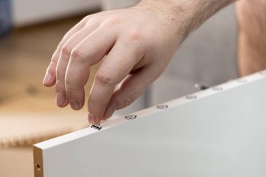 Bir insan elinin titizlikle küçük, şeffaf bir çıkartmayı mobilya montajı sırasında beyaz bir tahtaya sembollerle yapıştırması, dikkatle uygulanması ve akıllı ev gelişiminin altını çizmesi