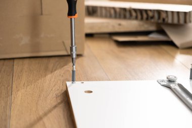 Turuncu saplı bir tornavidanın düz paket mobilya tahtasına vida takması ev yenileme sürecini ya da yeni apartman düzenini temsil ediyor.