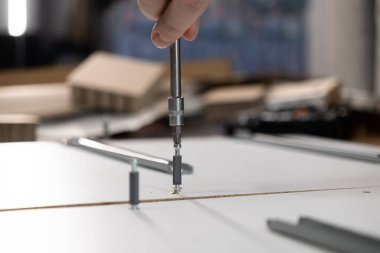 Güçlü bir tornavida aleti olan bir elin yakın çekimi, beyaz modüler mobilyaları titizlikle evde monte etmek, DIY projesinin başarısını ve verimliliğini vurgulamak