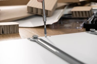 Yeni bir beyaz dolap paneline donanım takmak için elektrikli tornavida kullanan bir elin yakın çekimi, verimli bir ev yenilemesi ve inşaatı gösteriyor