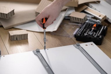 Beyaz mobilya montajı yapan bir kişinin yukarıdan aşağı görüntüsü, bir ev projesi için bir tornavida ve bir alet kutusu ile parçaların dikkatli kurulumunu vurguluyor