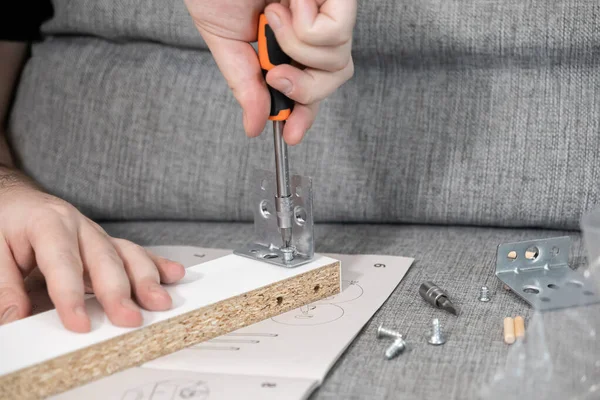 Tornavida kullanarak metal bir parçacığı parçacık tahtasına titizlikle yerleştiren ellerin yakın görüntüsü, adım adım mobilya montajını araçlarla ve kullanma kılavuzuyla gösteren