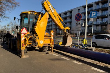 Poznan, Polonya - 18 Kasım 2025: Mor boru hattı yakınlarında kürekli sarı kepçe yükleyici, inşaat mühendisliği ve hayati kentsel hizmet geliştirme projelerini gösteriyor