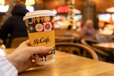 Poznan, Polonya - 19 Kasım 2025: Bulanık bir kafe ortamında keyifli bir anın tadını çıkaran tek kullanımlık McCafe kahve bardağını tutmak