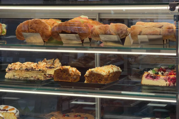 Yeni hazırlanmış hamur işleri, çeşitli kekler ve perakende satışlar için cam ekran içinde birden fazla rafa dizilmiş sandviçler.