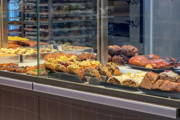 Taze pişmiş tatlı hamur işleri, çikolatalı kruvasanlar, bozulmuş browniler ve perakende cam bir kutuda cazip bir şekilde sergilenen kremalı çörekler.
