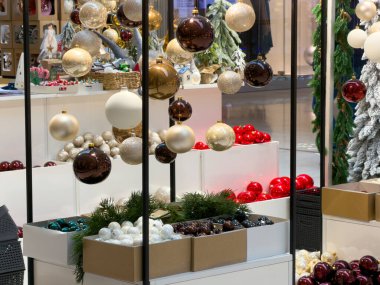 Mağaza vitrininde altın, kahverengi, beyaz ve kırmızı renkli parlak Noel mücevherleri, bayram alışverişi ve mevsimlik dekorasyon için ilham verici müşteriler yer alıyor.