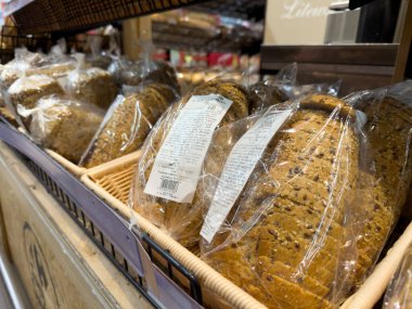 Poznan, Polonya - 28 Kasım 2025: Taze tahıllı ekmek somunları, önceden dilimlenmiş ve plastik paketlenmiş, perakende raflarındaki hasır sepetlerde düzenli olarak düzenlenmiş, sağlıklı günlük yiyecek alışverişini teşvik eden