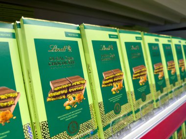 Poznan, Polonya - 28 Kasım 2025: Çok sayıda yeşil ve altın ambalajlı Lindt Dubai tarzı çikolatalar parlak ışıklandırılmış bir market rafında açıkça görülebilmektedir